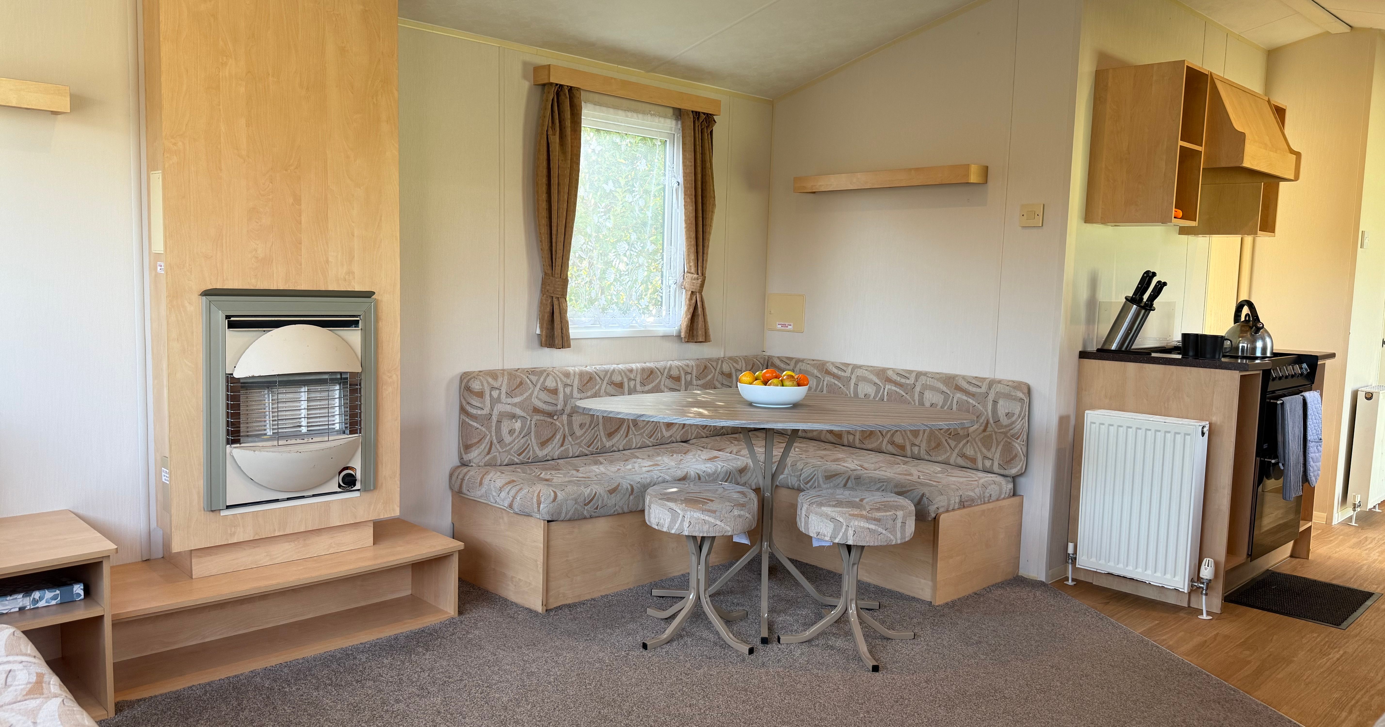 Interior of a cozy mobile home with a dining nook, heater, and kitchen area.