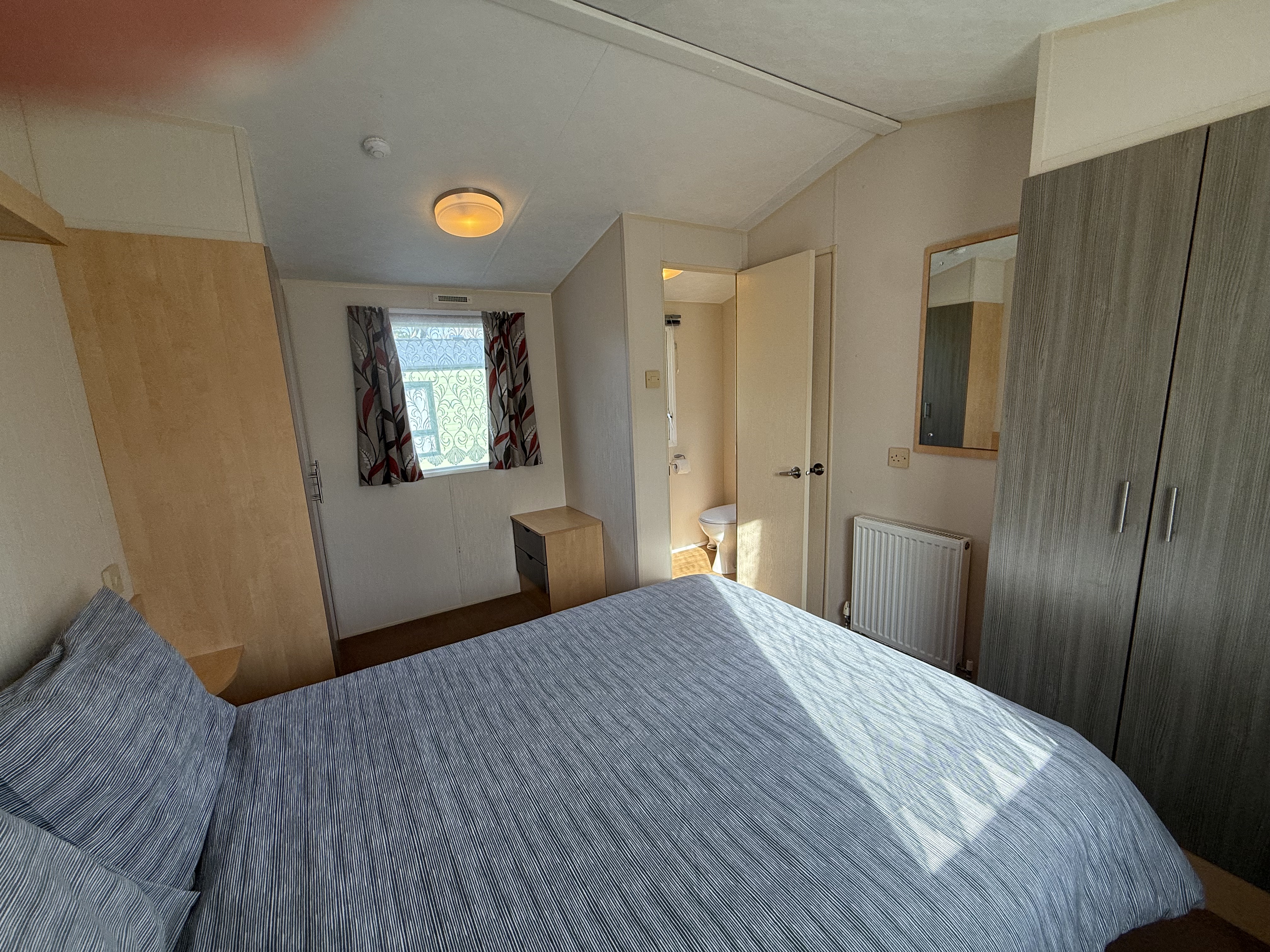 A small, well-lit bedroom with a bed, wardrobe, and en suite bathroom.