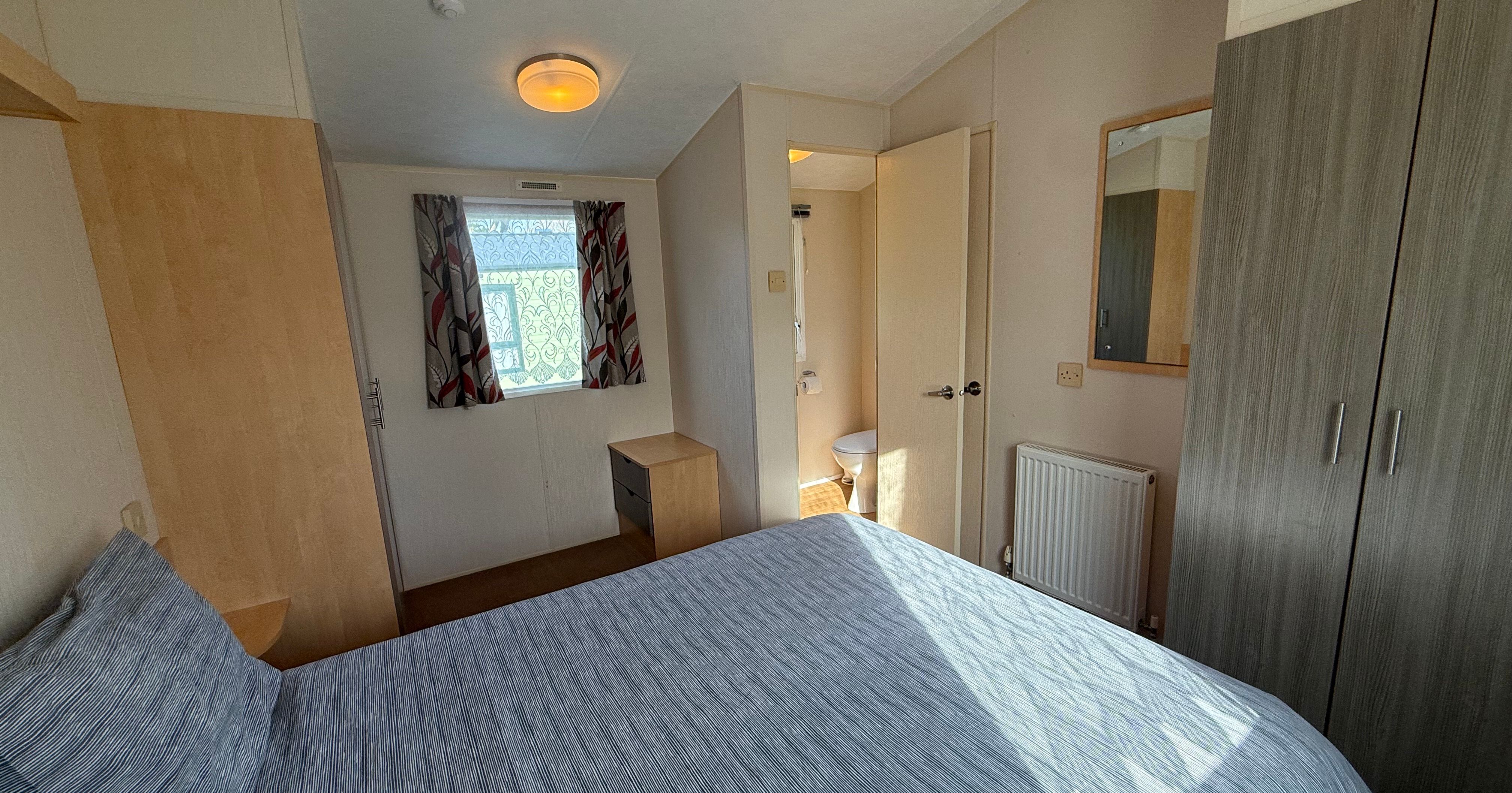 A small, well-lit bedroom with a bed, wardrobe, and en suite bathroom.