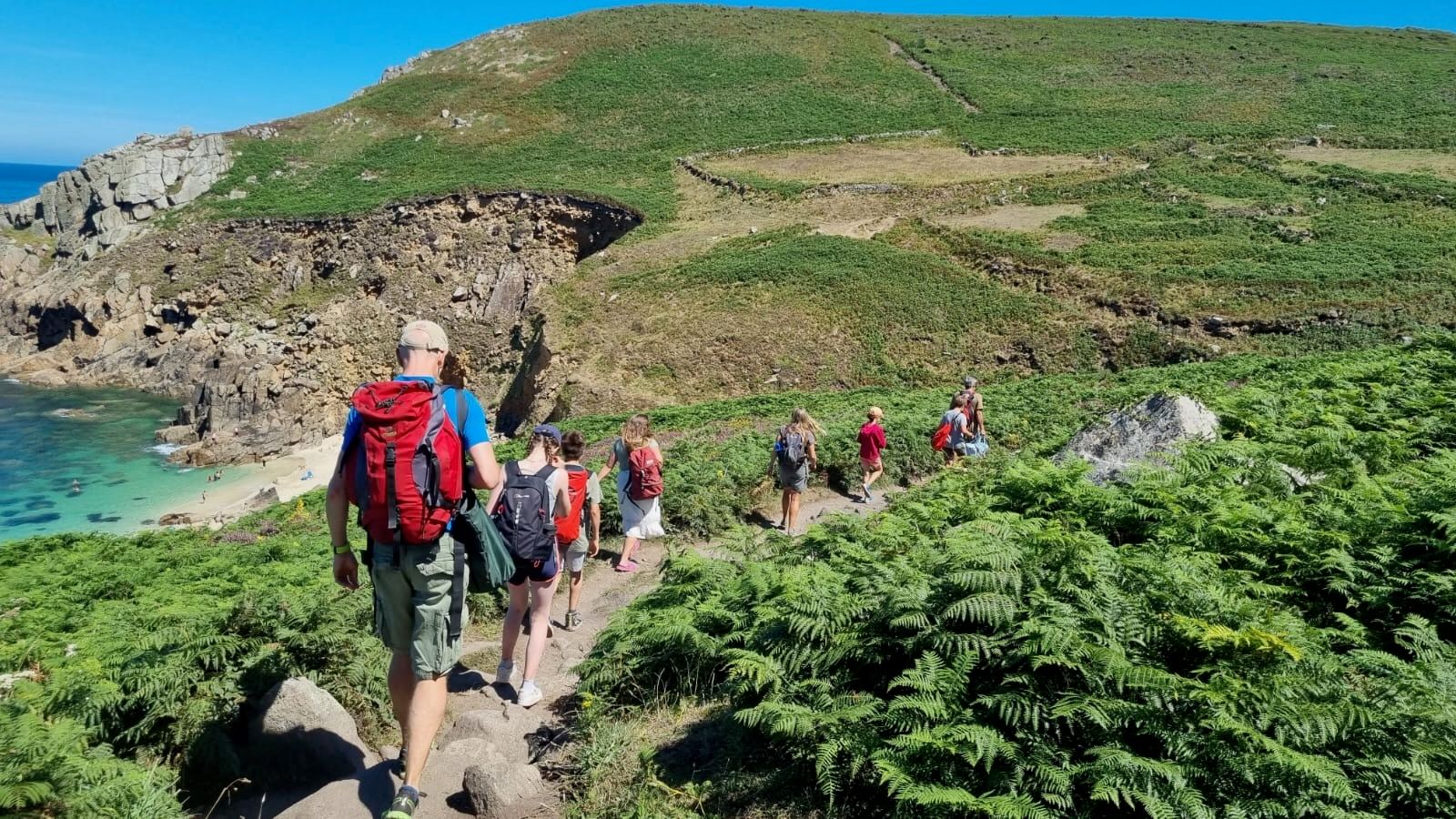 Group of hikers walking along a coastal path by Portherris Beach, surrounded by green hills and cliffs.