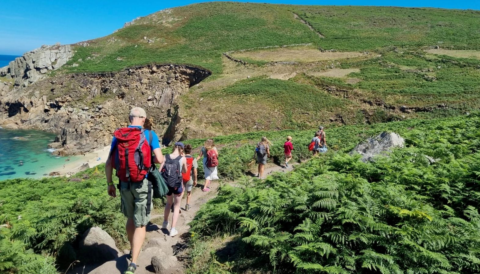 Group of hikers walking along a coastal path by Portherris Beach, surrounded by green hills and cliffs.