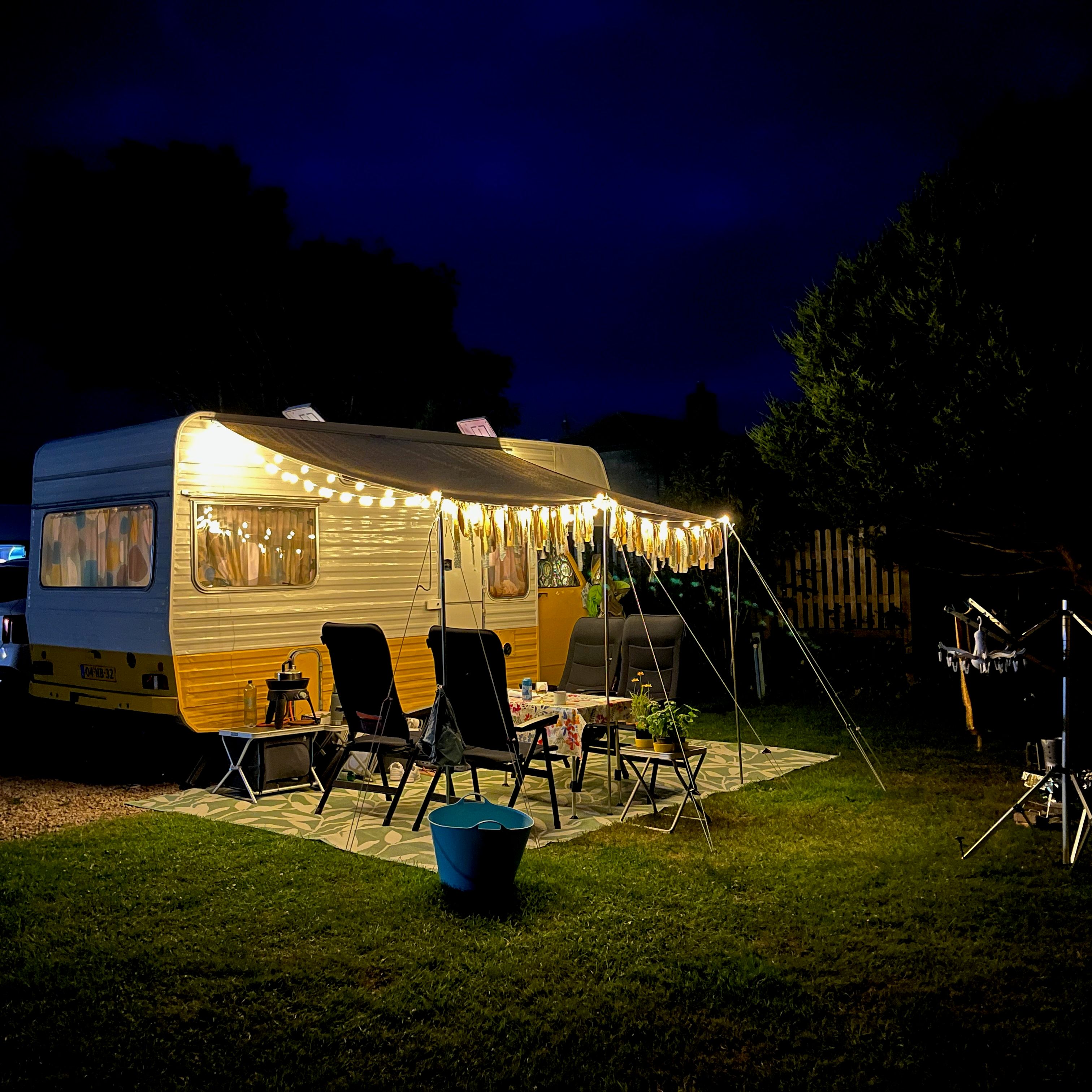 Cozy camping setup with a vintage caravan illuminated by string lights at night.