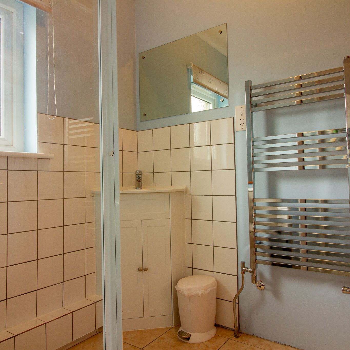 Modern bathroom with white tiles, vanity unit, trash bin, mirror, heated towel rail and window