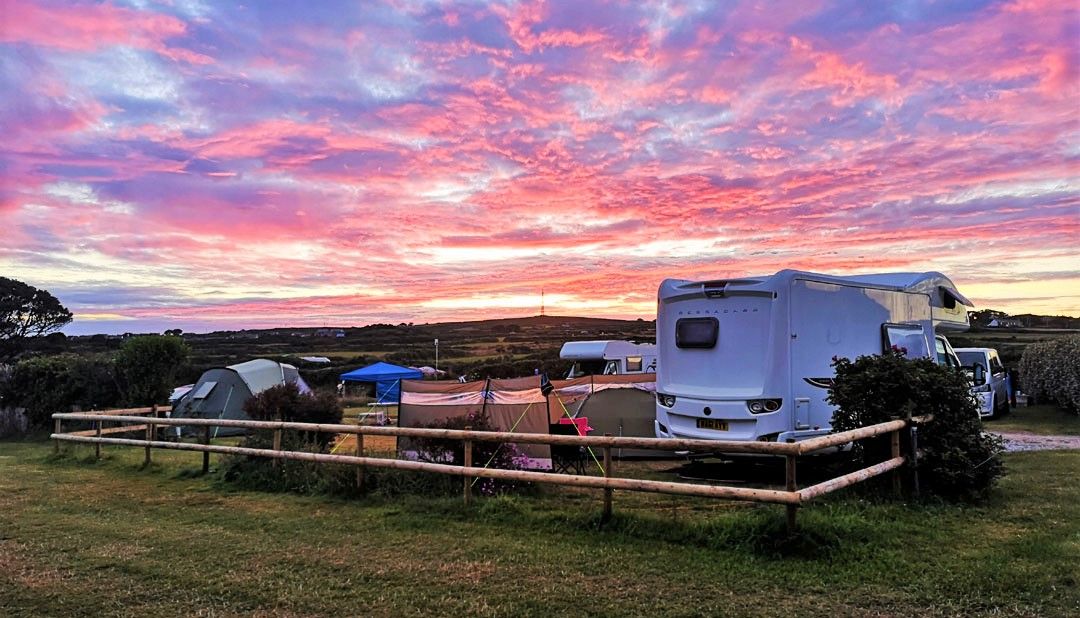 A vibrant sunrise over a campsite with tents, a camper van, and grassy fields.