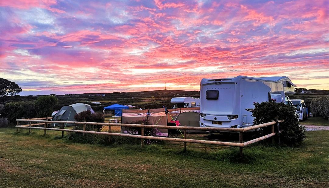 A vibrant sunrise over a campsite with tents, a camper van, and grassy fields.