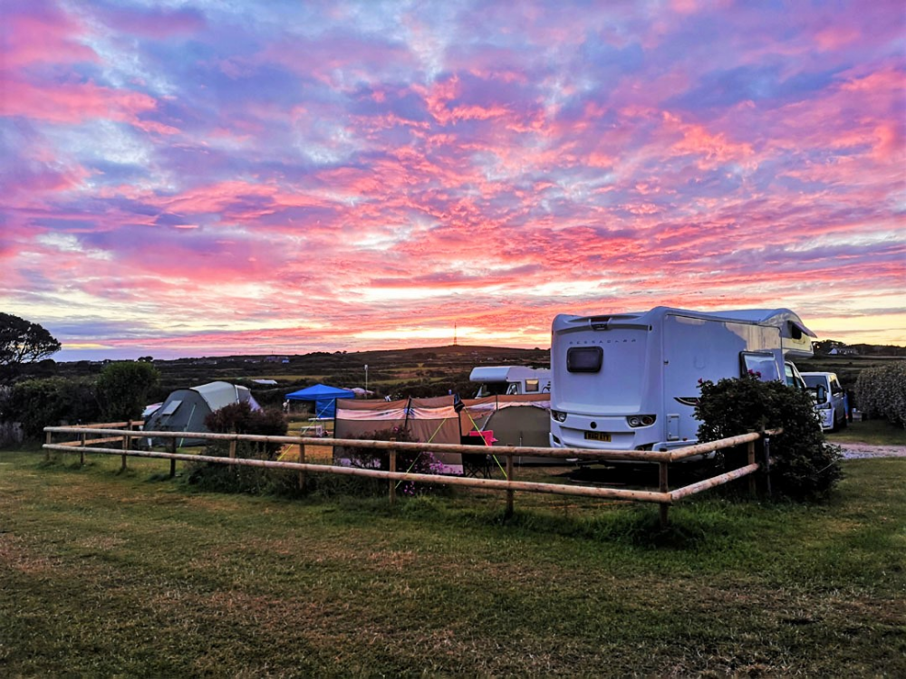 A vibrant sunrise over a campsite with tents, a camper van, and grassy fields.