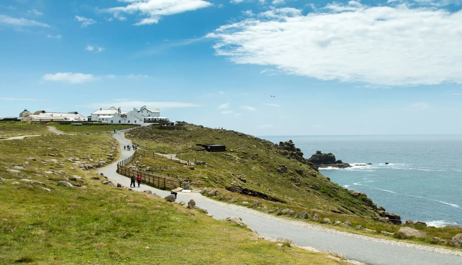 Coastal path leading to white buildings on a grassy hill overlooking the sea