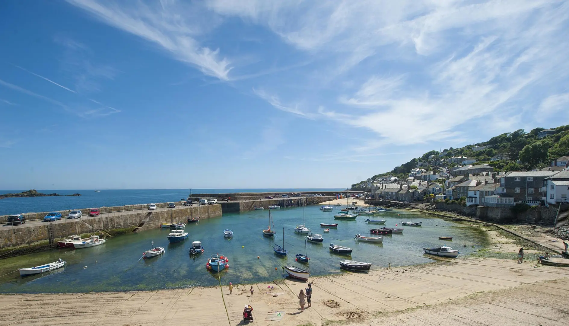 Picturesque coastal harbor with small boats, sandy beach, and seaside village