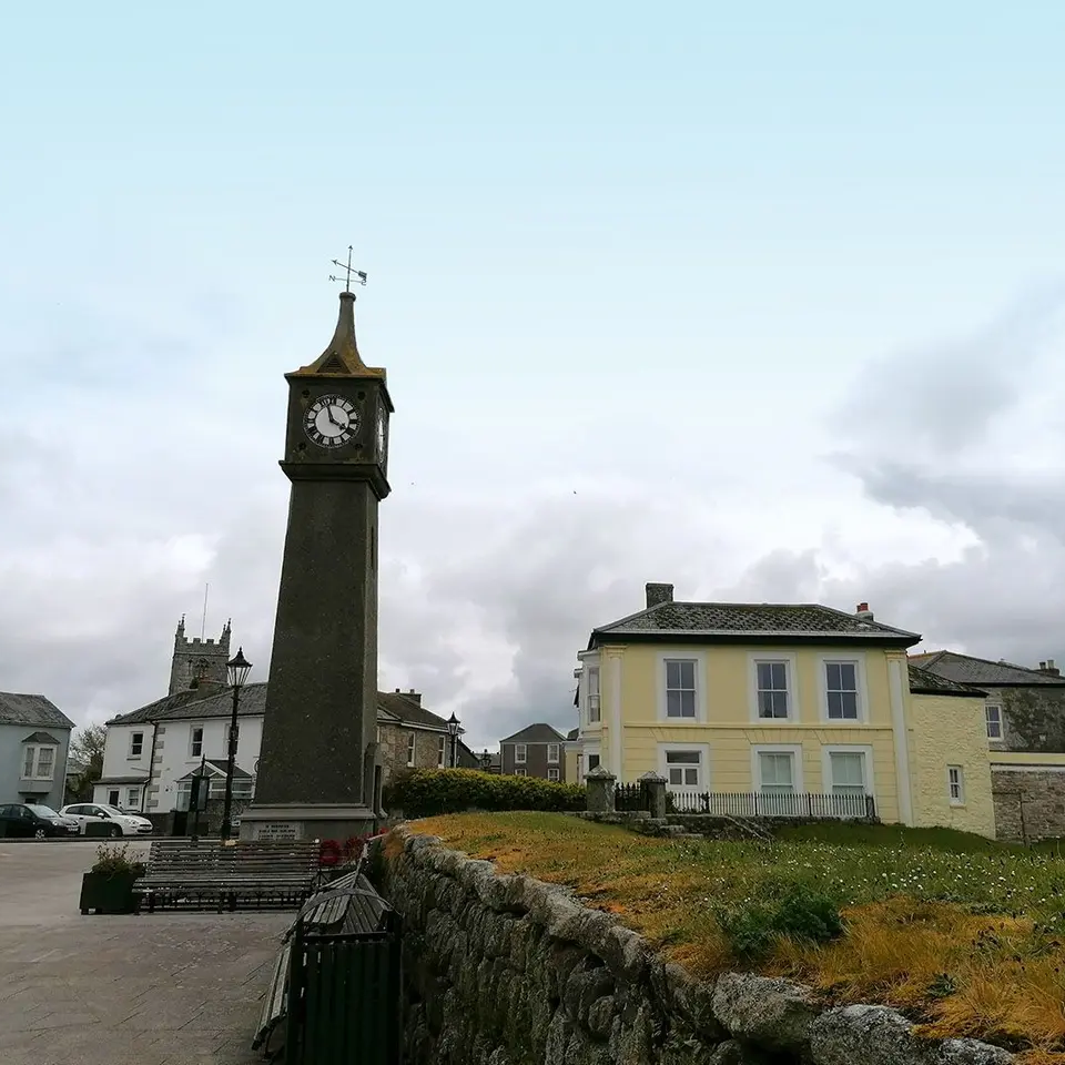 Town square with a tall clock tower and surrounding buildings under a cloudy sky