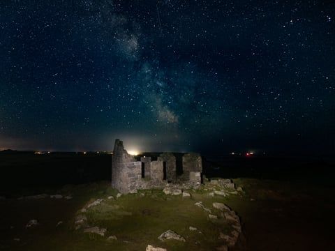 Old stone ruins illuminated at night under a star-filled sky with the Milky Way visible.