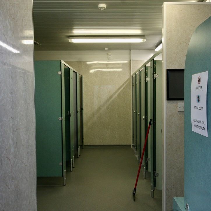 Interior view of a public restroom with several green stall doors and a cleaning mop leaning against the wall.