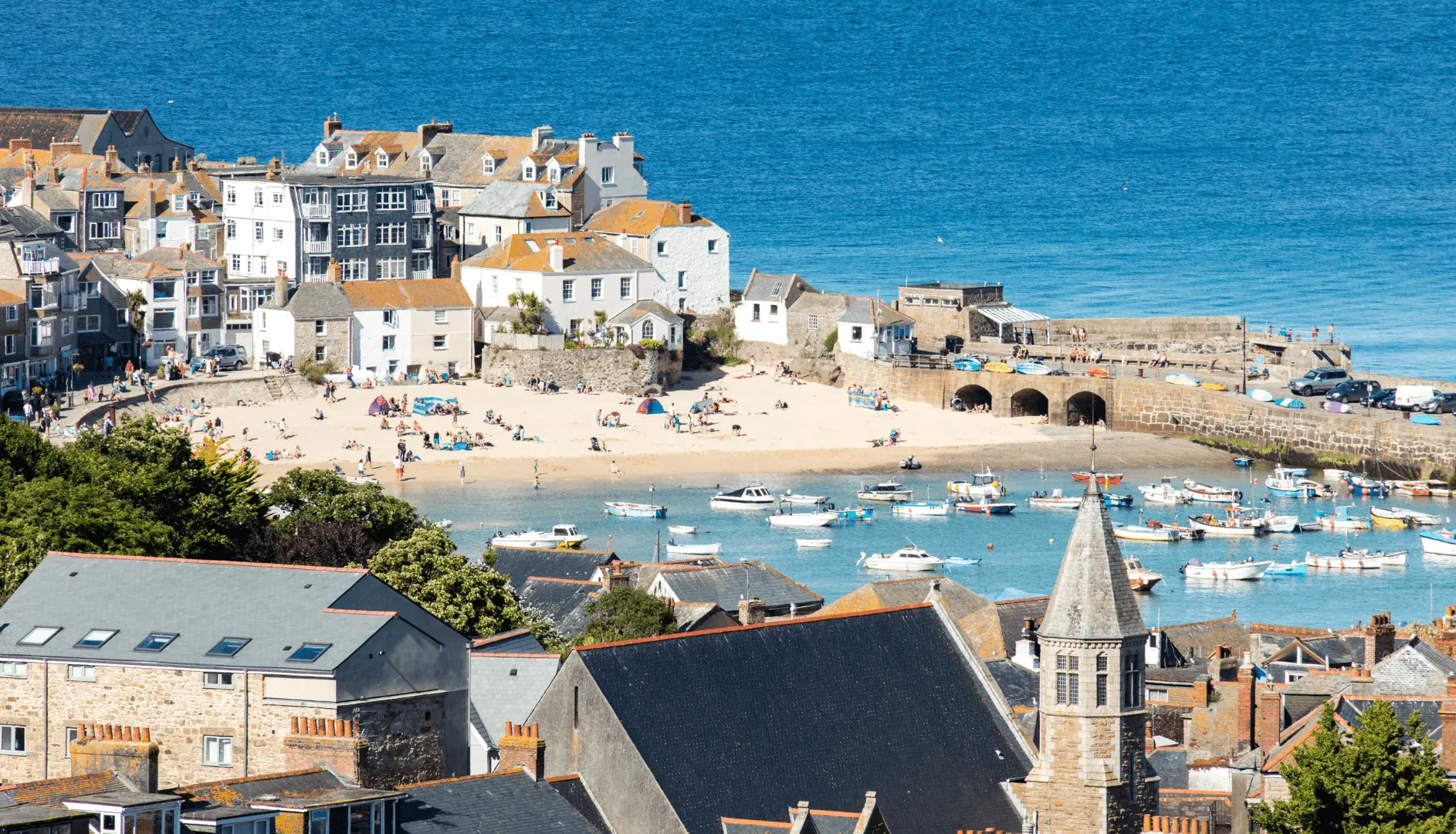 Coastal town with a sandy beach, boats in the harbor, and historic buildings by the sea
