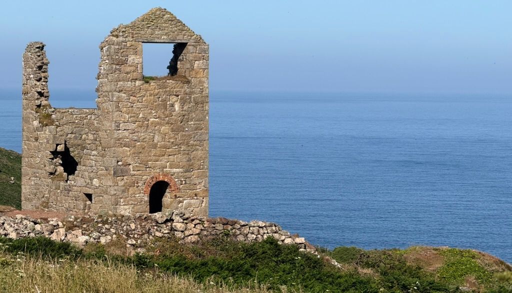 Ruins of an old stone building on a grassy hill overlooking the sea