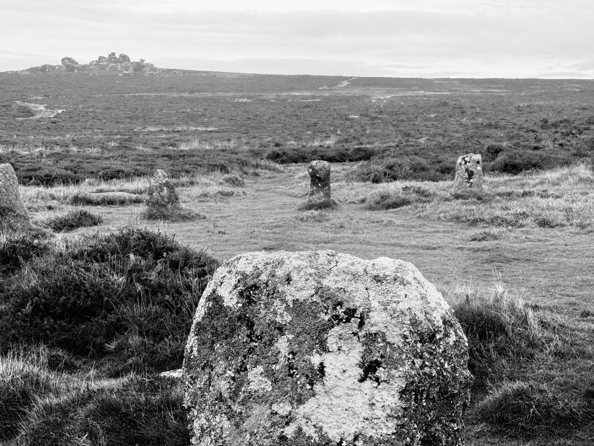 A black and white photo of a mossy standing stone in a grassy field with several other stones in the background.