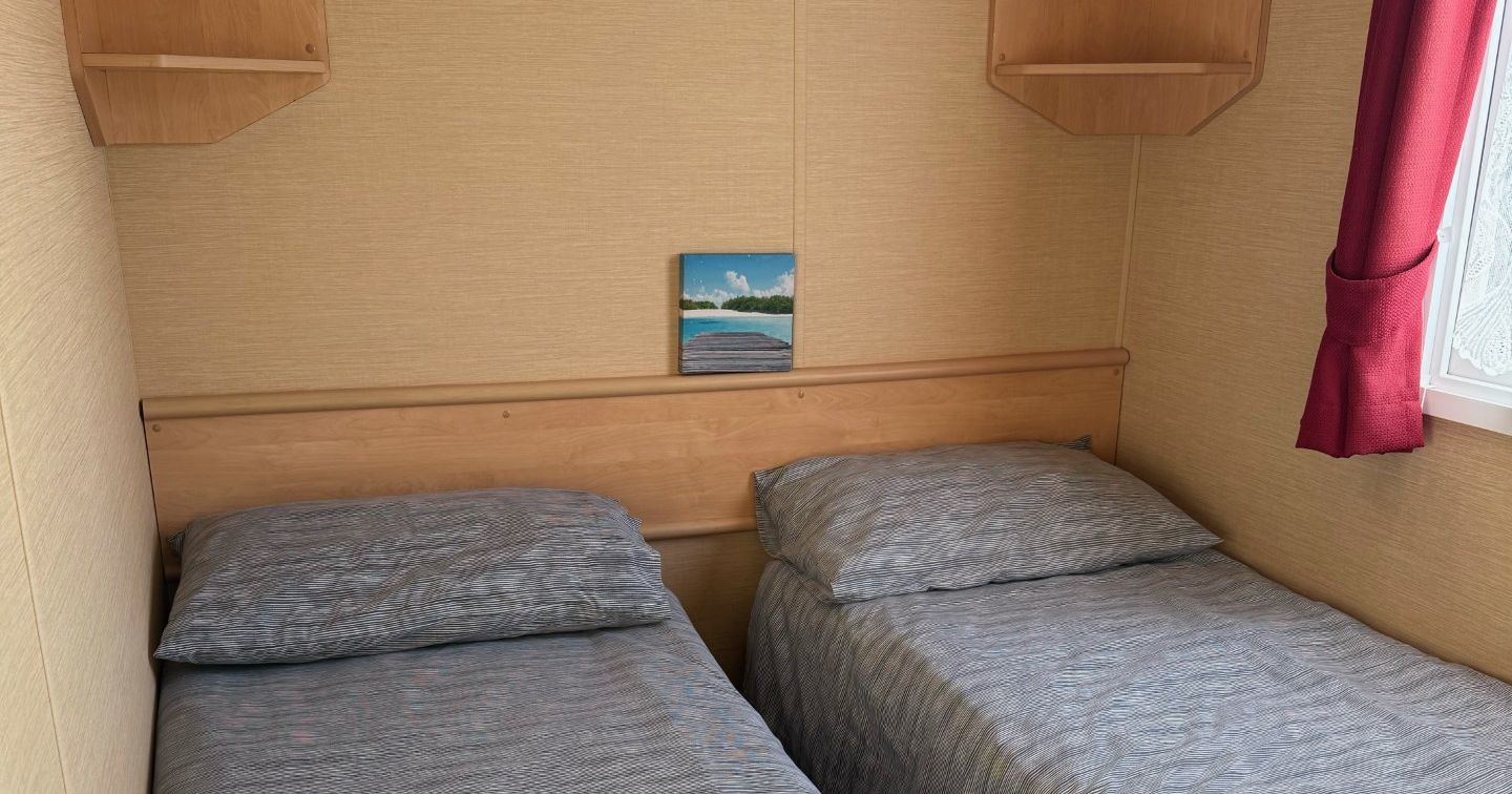 Small bedroom with two single beds, light wood shelves, and a window with red curtains.