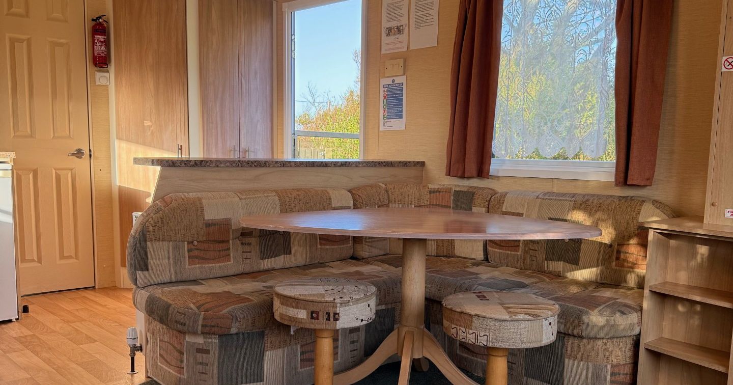 Interior of a cozy mobile home dining area with a round table, built-in cushioned seating, and two round stools.