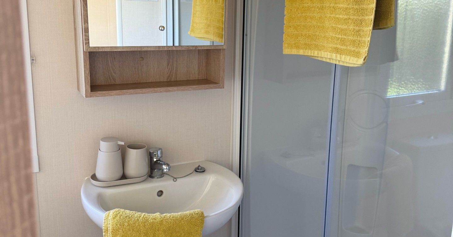 Small bathroom with a shower, pedestal sink, mirror cabinet, and yellow towels.