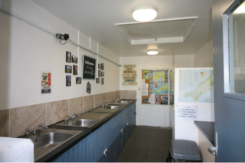 Communal kitchen and washing area with multiple sinks, bulletin boards, and maps on the walls.