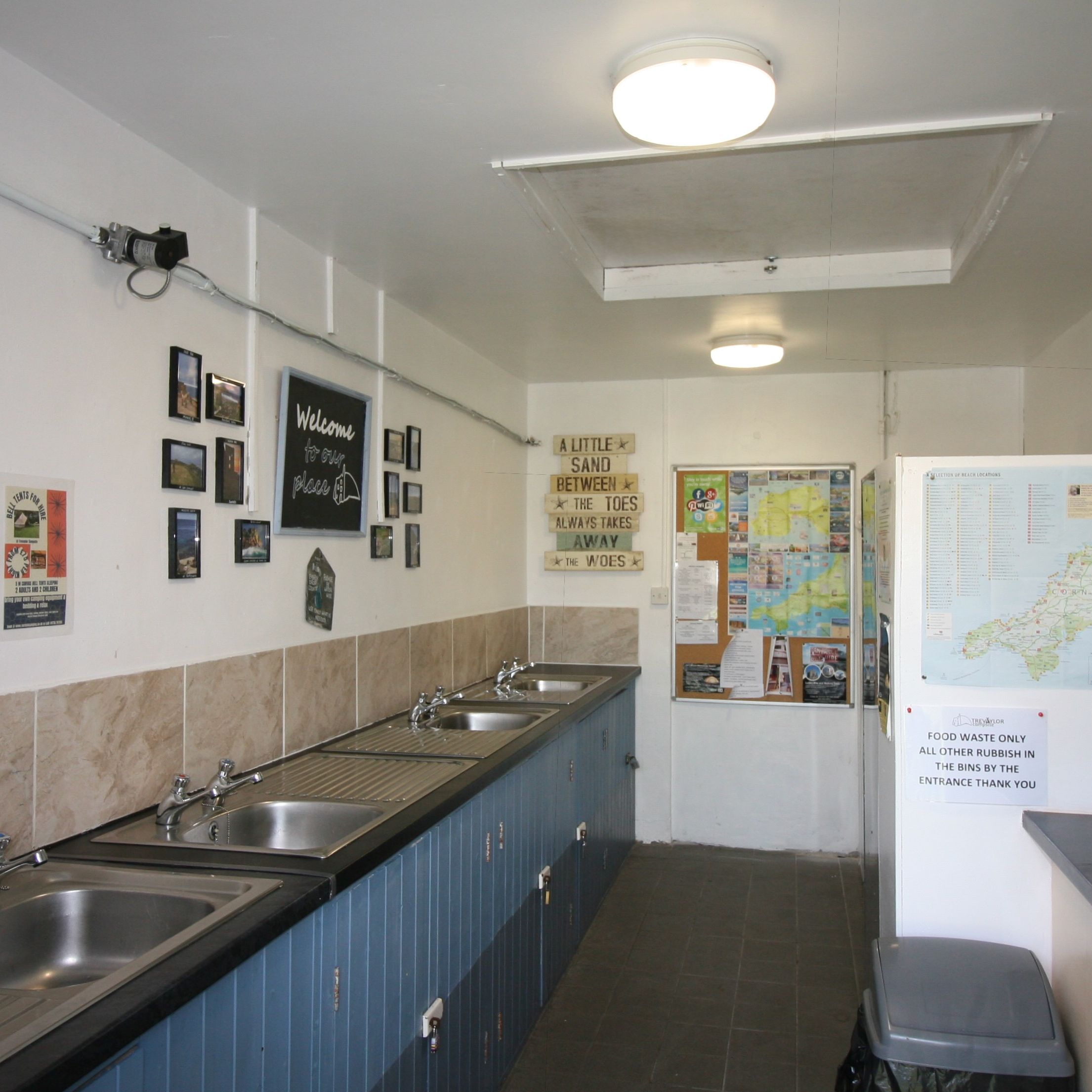 Communal kitchen and washing area with multiple sinks, bulletin boards, and maps on the walls.