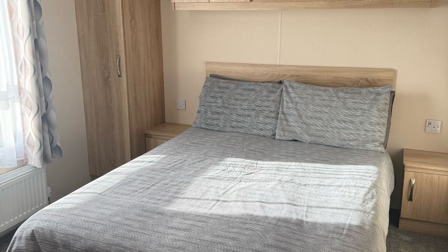 A tidy bedroom with a double bed, wooden wardrobes, and overhead cabinets.