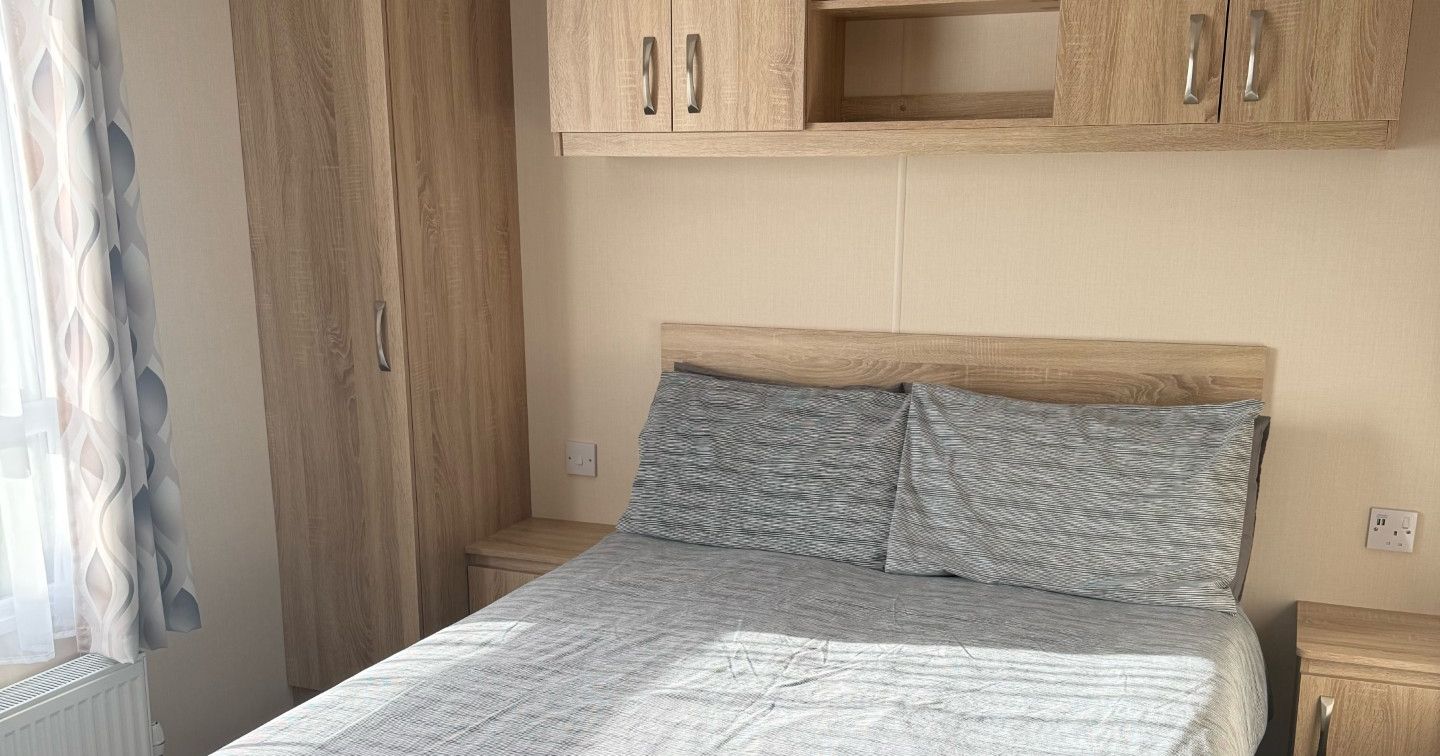 A tidy bedroom with a double bed, wooden wardrobes, and overhead cabinets.