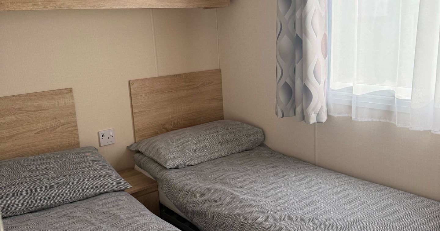 Small bedroom with two single beds, wooden cabinets, and a window with patterned curtains.