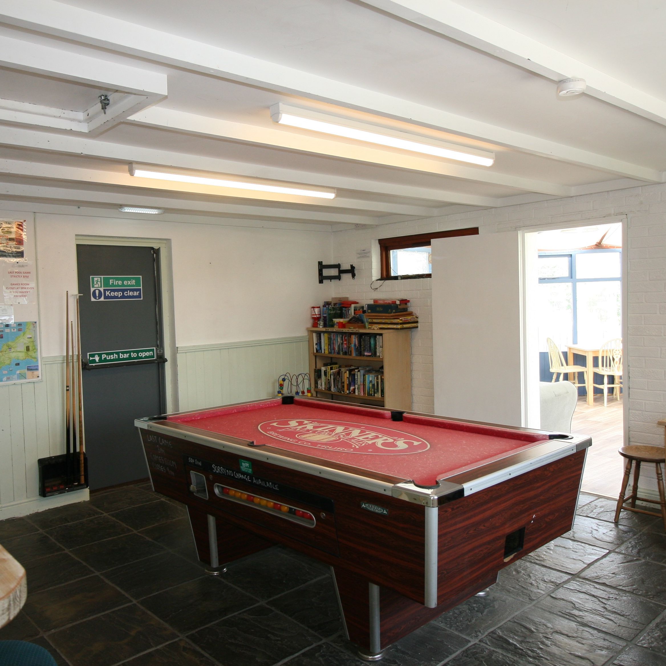 A recreational room with a pool table, bookshelf, tables, and stools.