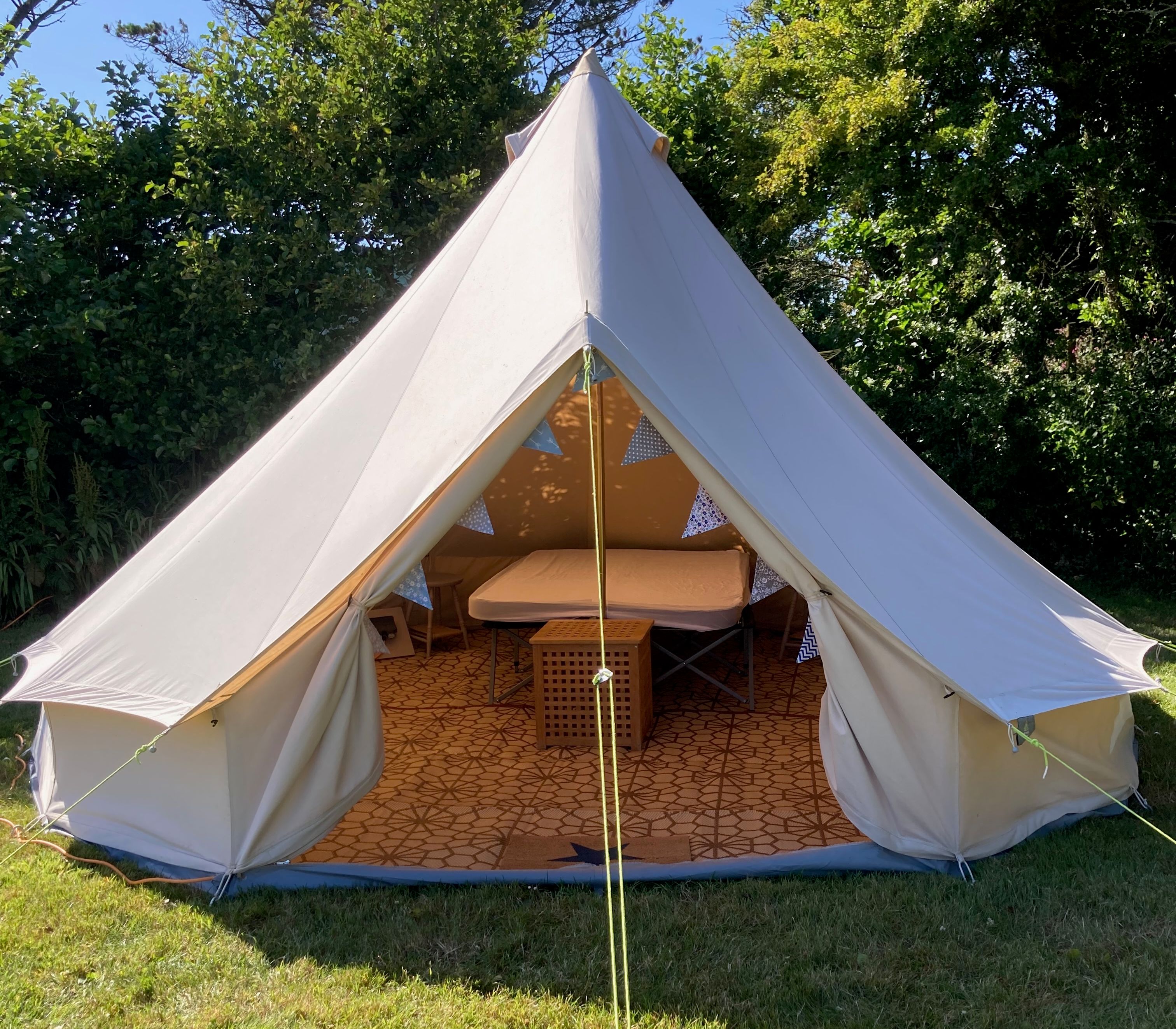 A large bell tent set up on a grassy area, with the entrance open to show a neatly arranged interior.