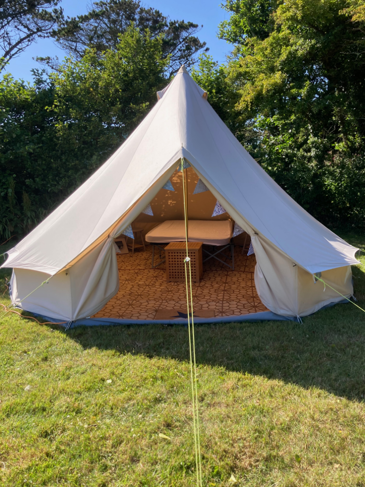 A large bell tent set up on a grassy area, with the entrance open to show a neatly arranged interior.