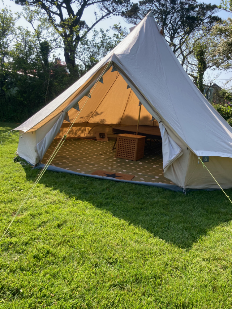 A large canvas tent set up on grass with its front flap open, revealing furniture inside.