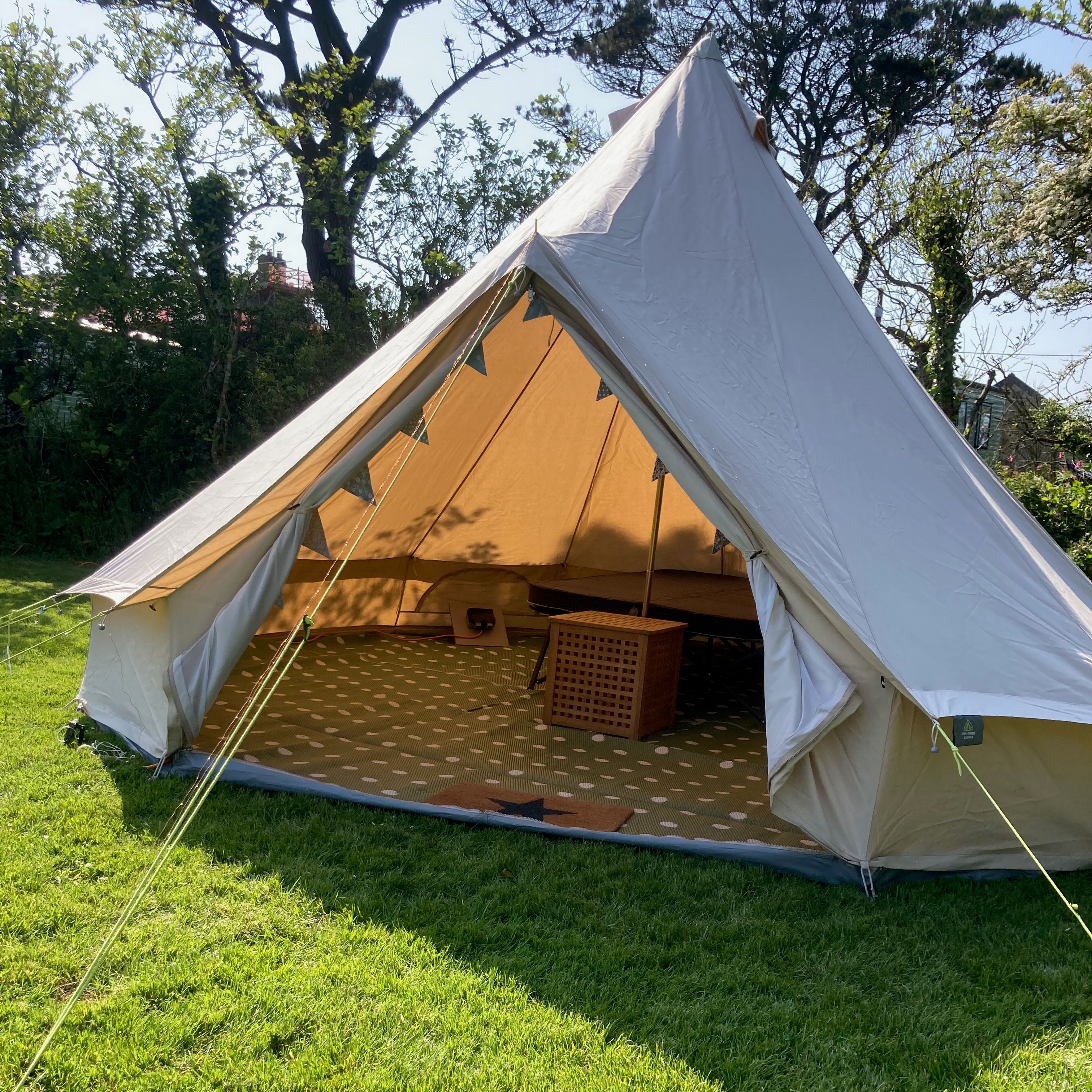 A large canvas tent set up on grass with its front flap open, revealing furniture inside.