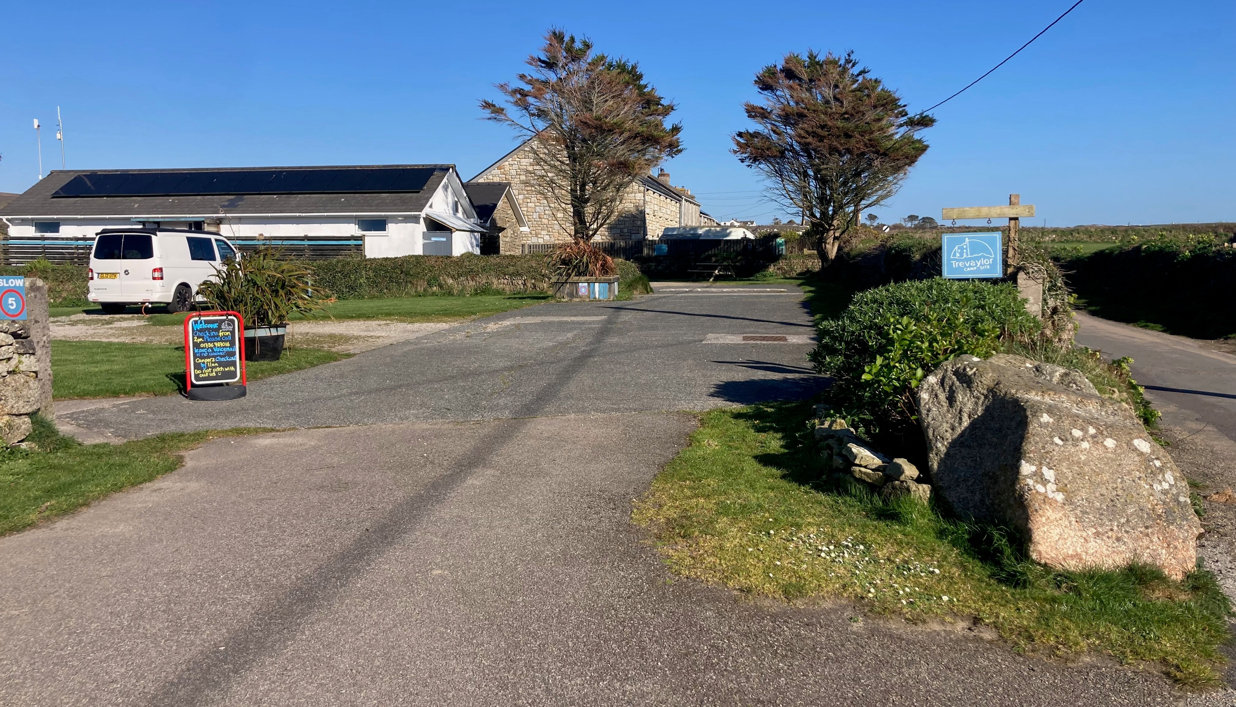 Country lane leading to a building complex, with a sign for Trevaylor Caravan & Camping Park and a van parked near a board.