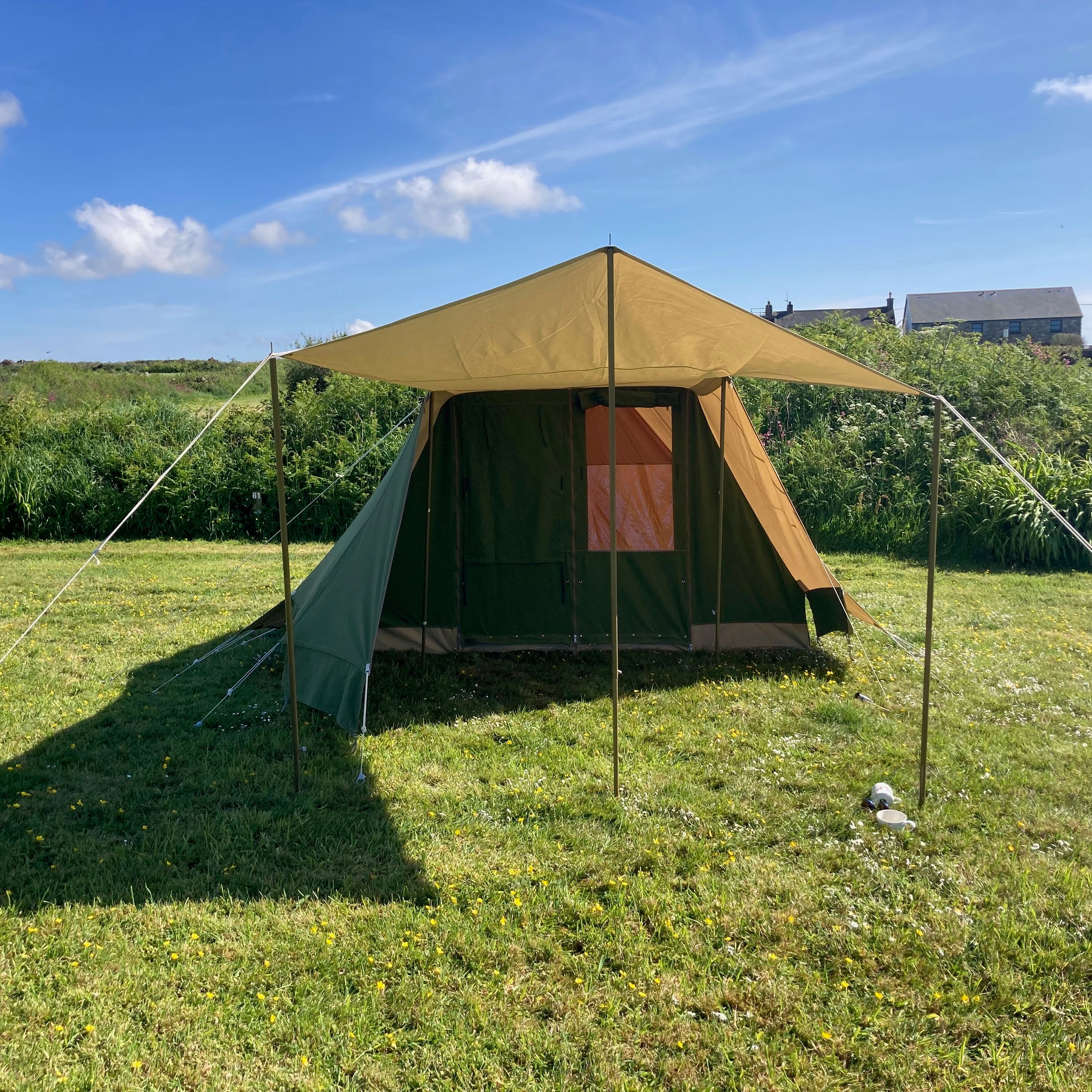 Large green and brown canvas tent set up on grassy field under a clear blue sky.