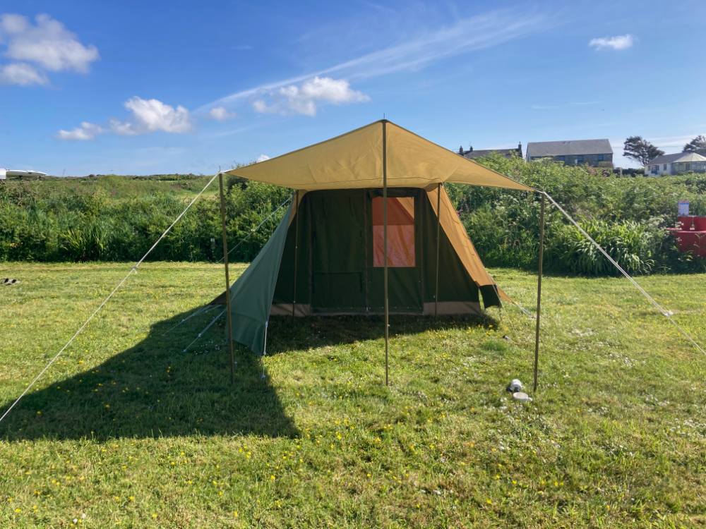 Large green and brown canvas tent set up on grassy field under a clear blue sky.