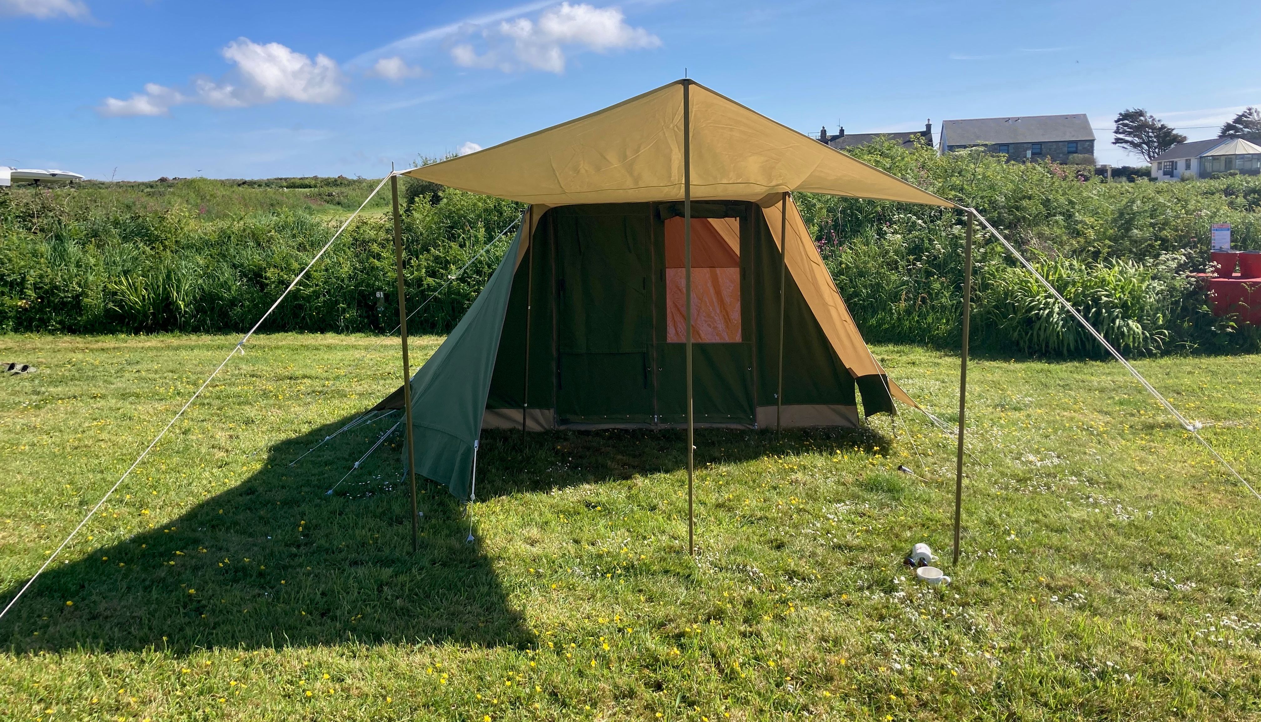 Large green and brown canvas tent set up on grassy field under a clear blue sky.