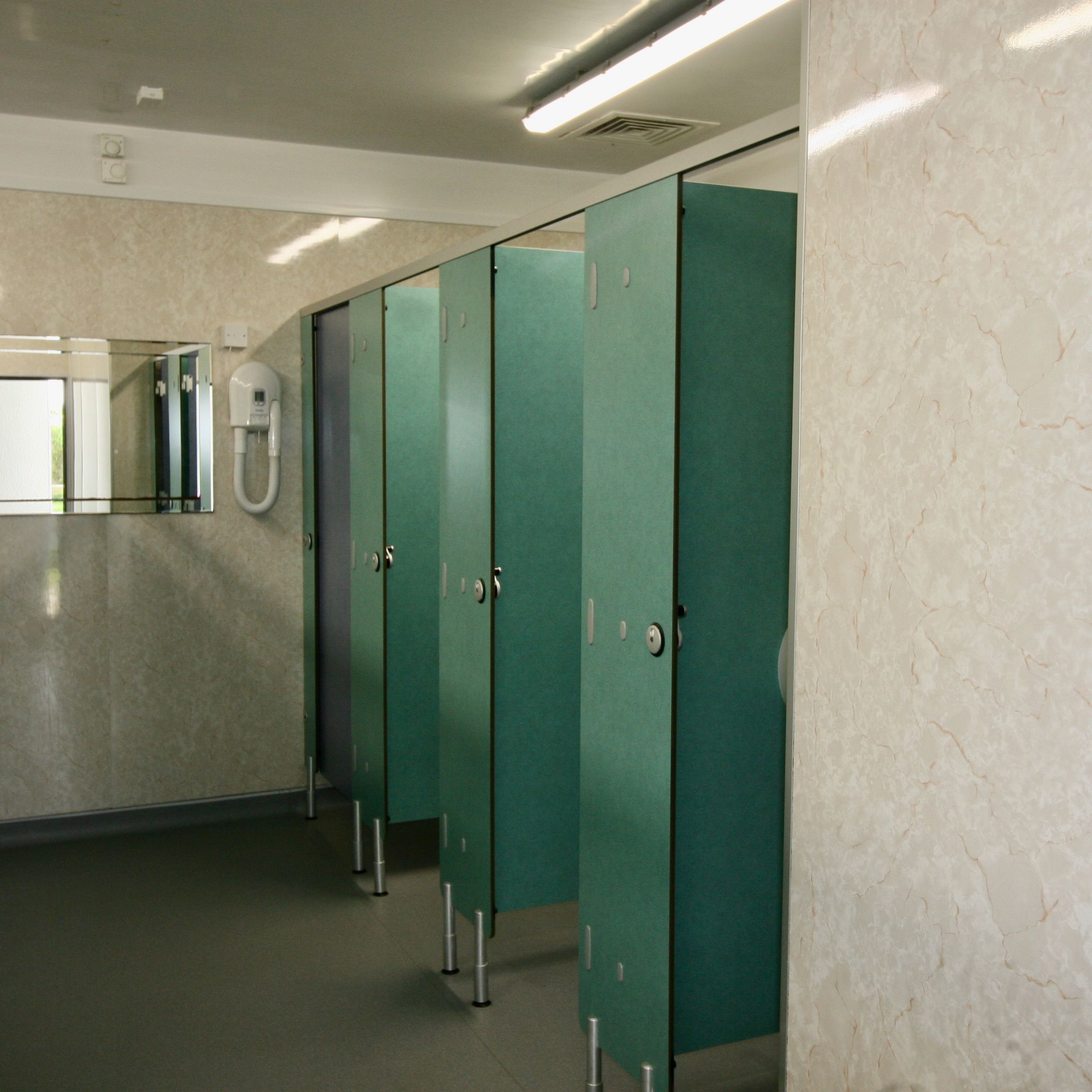 Public restroom with green stall doors, a wall mirror, and a hand dryer.