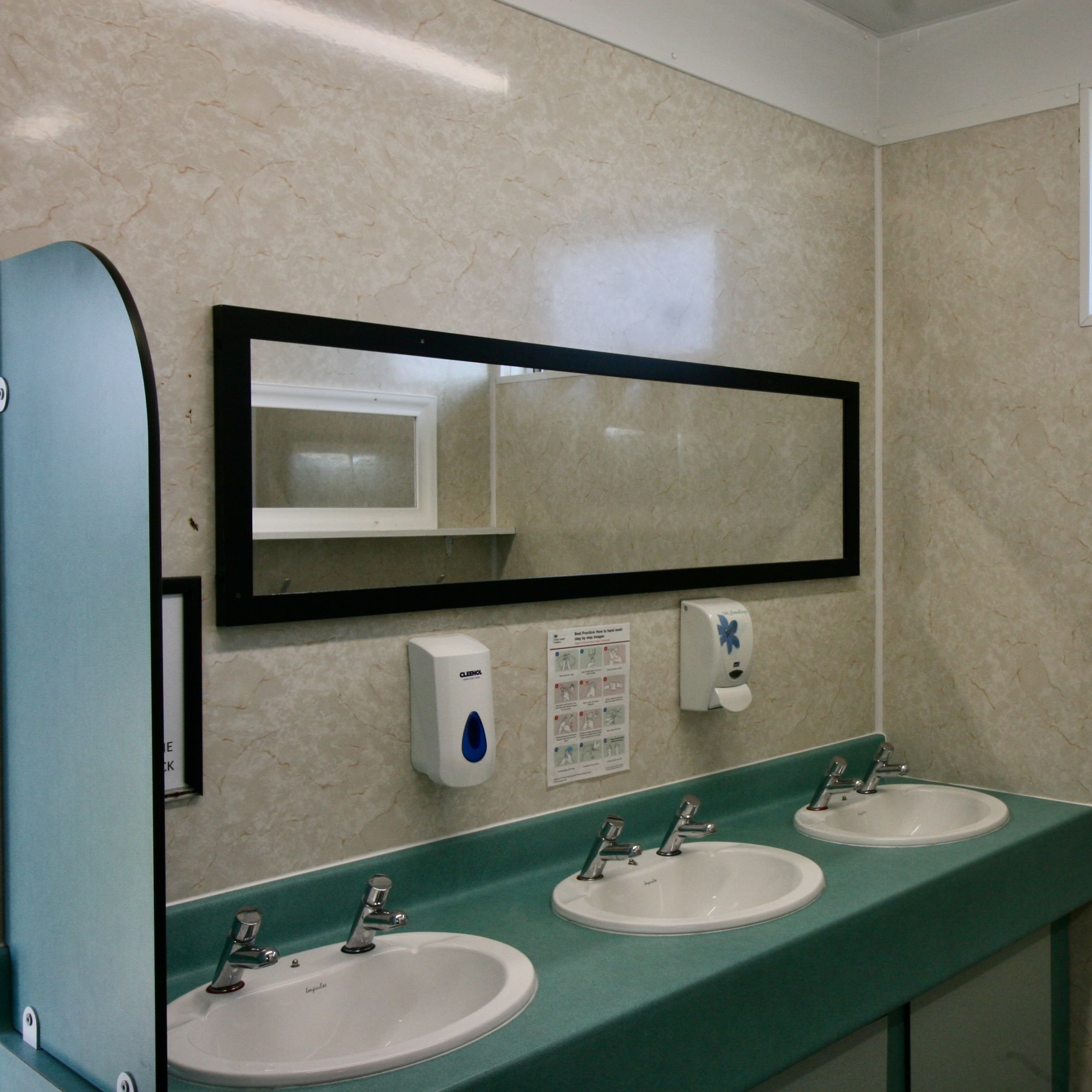 Public restroom with three sinks, soap dispensers, a rectangular mirror, and a small window.