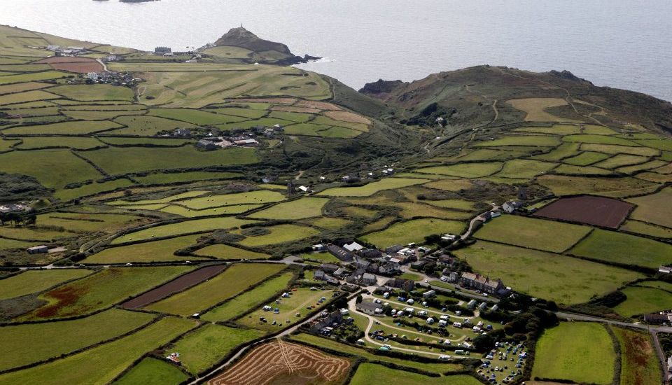 Aerial view of patchwork green fields, a coastal village, and the sea beyond.