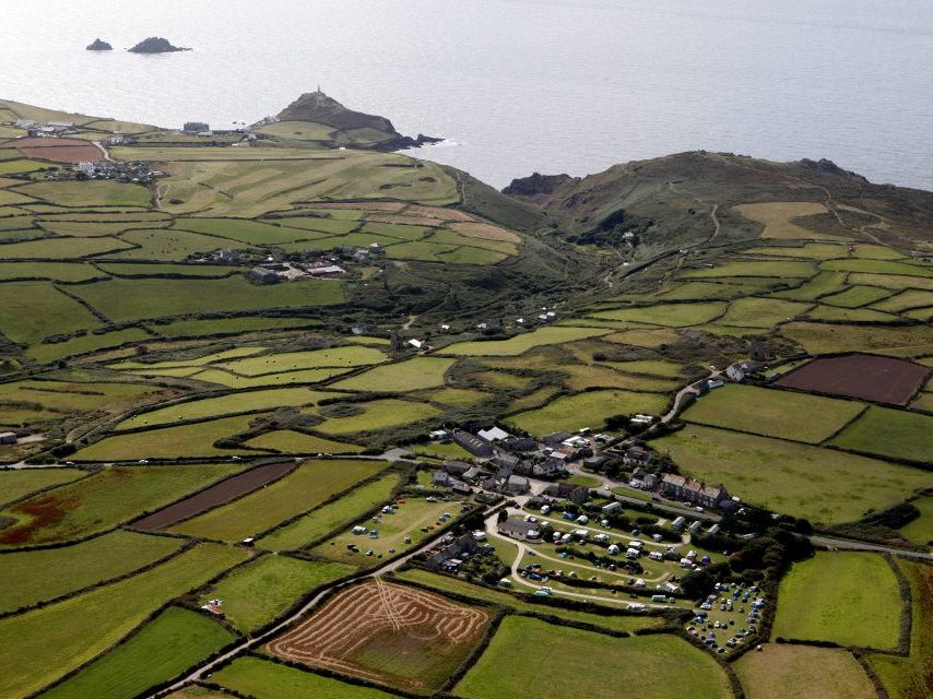 Aerial view of patchwork green fields, a coastal village, and the sea beyond.