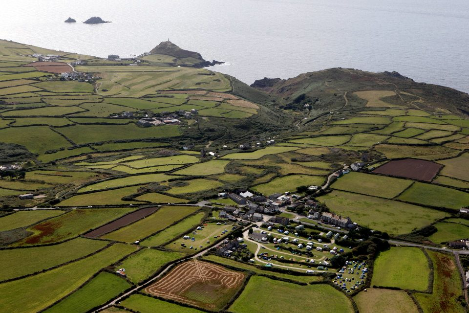 Aerial view of patchwork green fields, a coastal village, and the sea beyond.