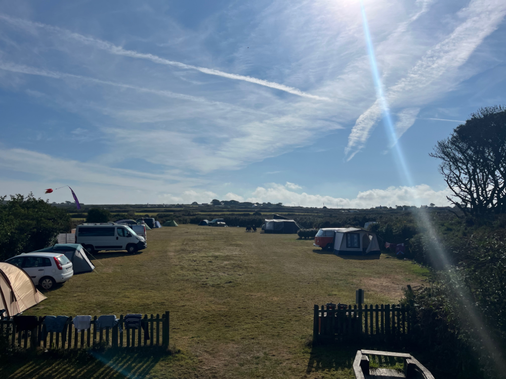 Campsite with tents, campervans, and cars under a sunny sky with wispy clouds