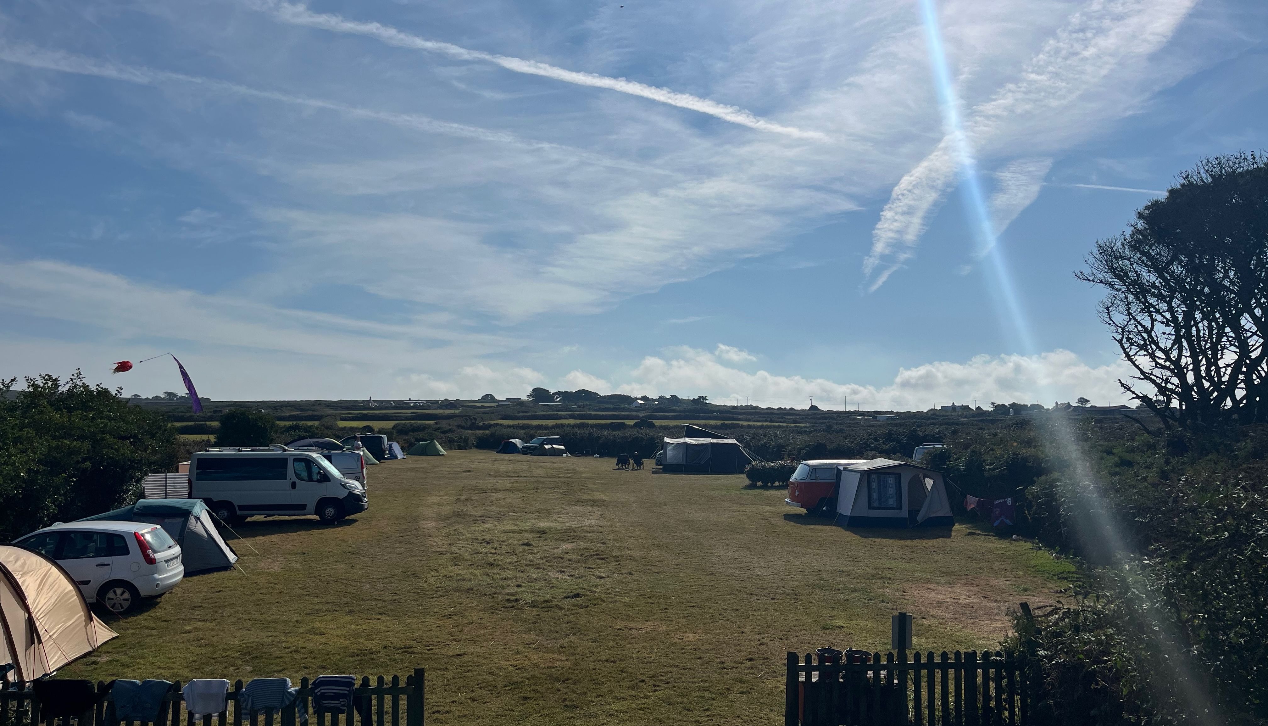 Campsite with tents, campervans, and cars under a sunny sky with wispy clouds