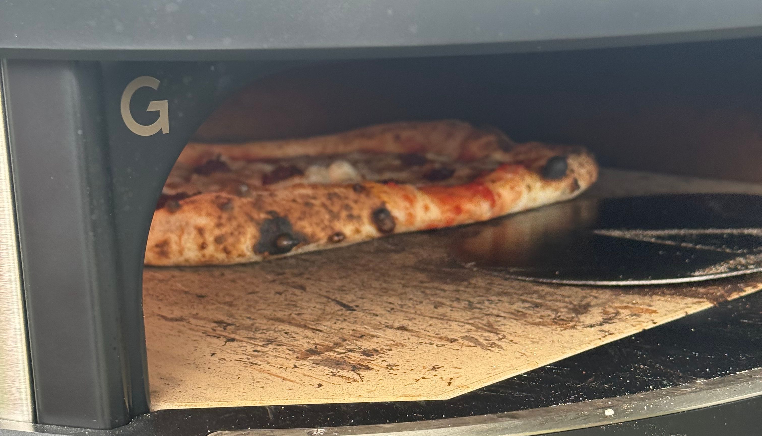 A pizza cooking inside a black outdoor pizza oven