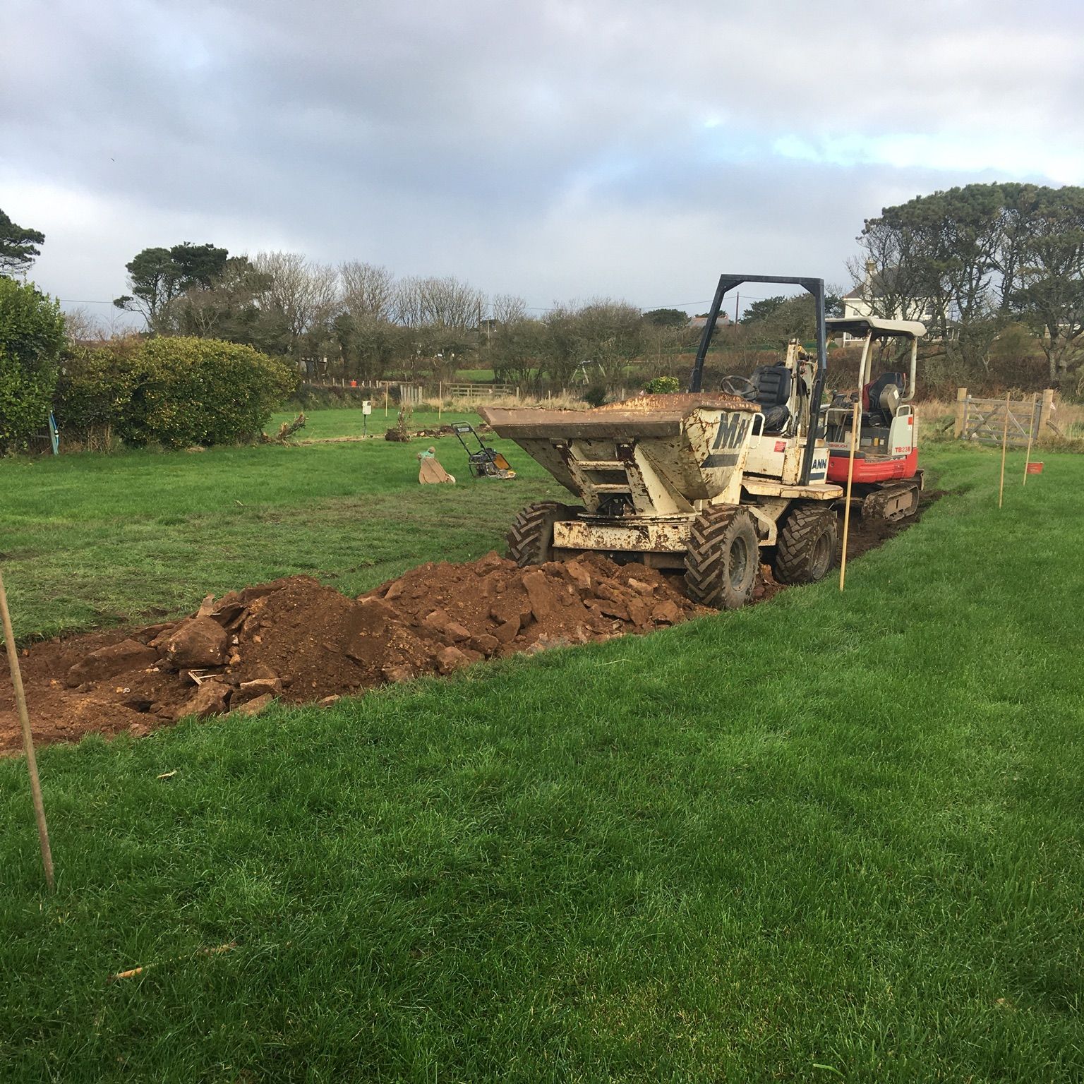 Excavator digging a trench in a grassy field