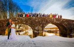 Maggie McCall - bride and groom in snow with guests on bridge