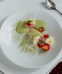 Gourmet dessert with green and red accents on a white plate, served with a glass of white wine