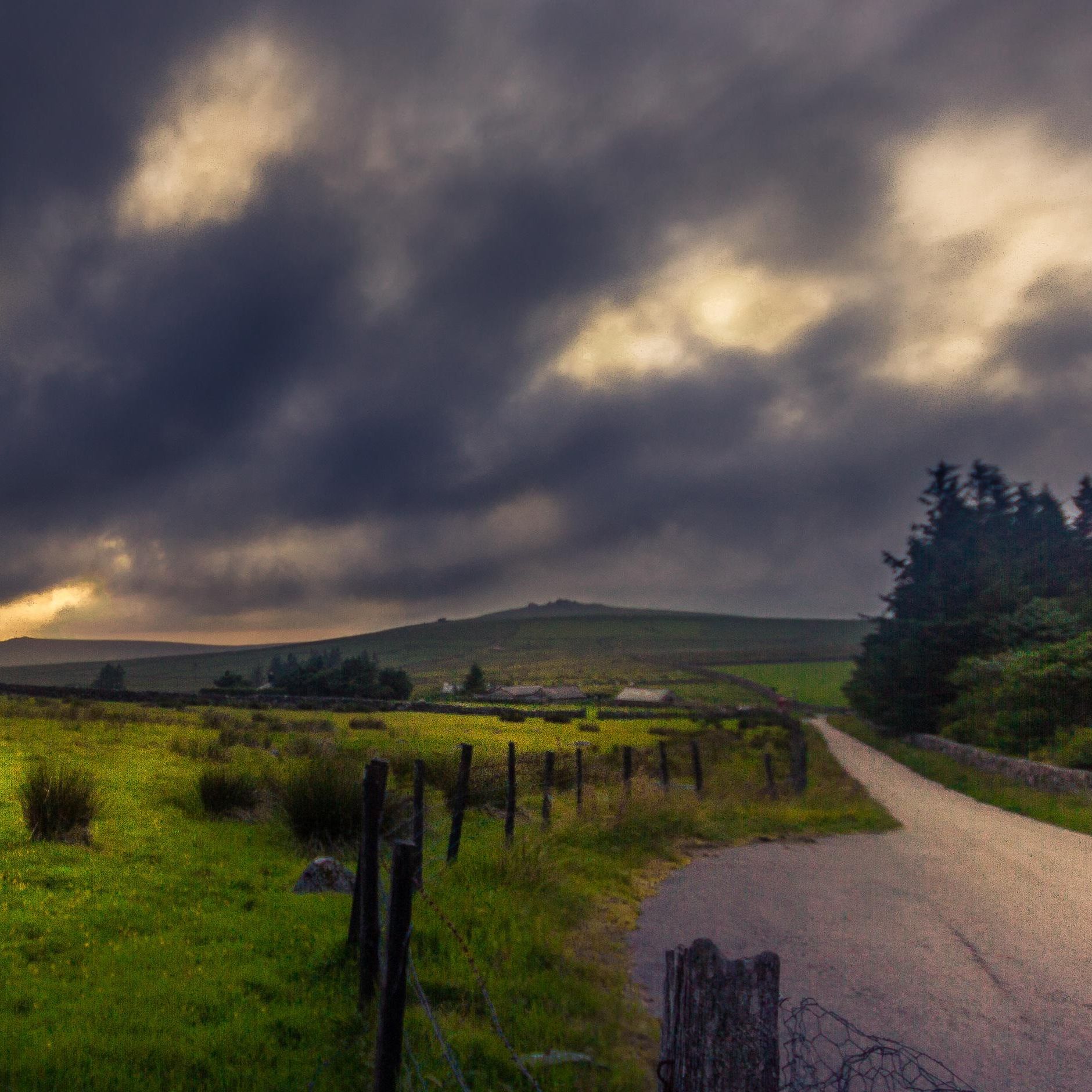 Stormy clouds over a rural landscape with a winding road and stone fence