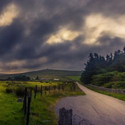 Stormy clouds over a rural landscape with a winding road and stone fence