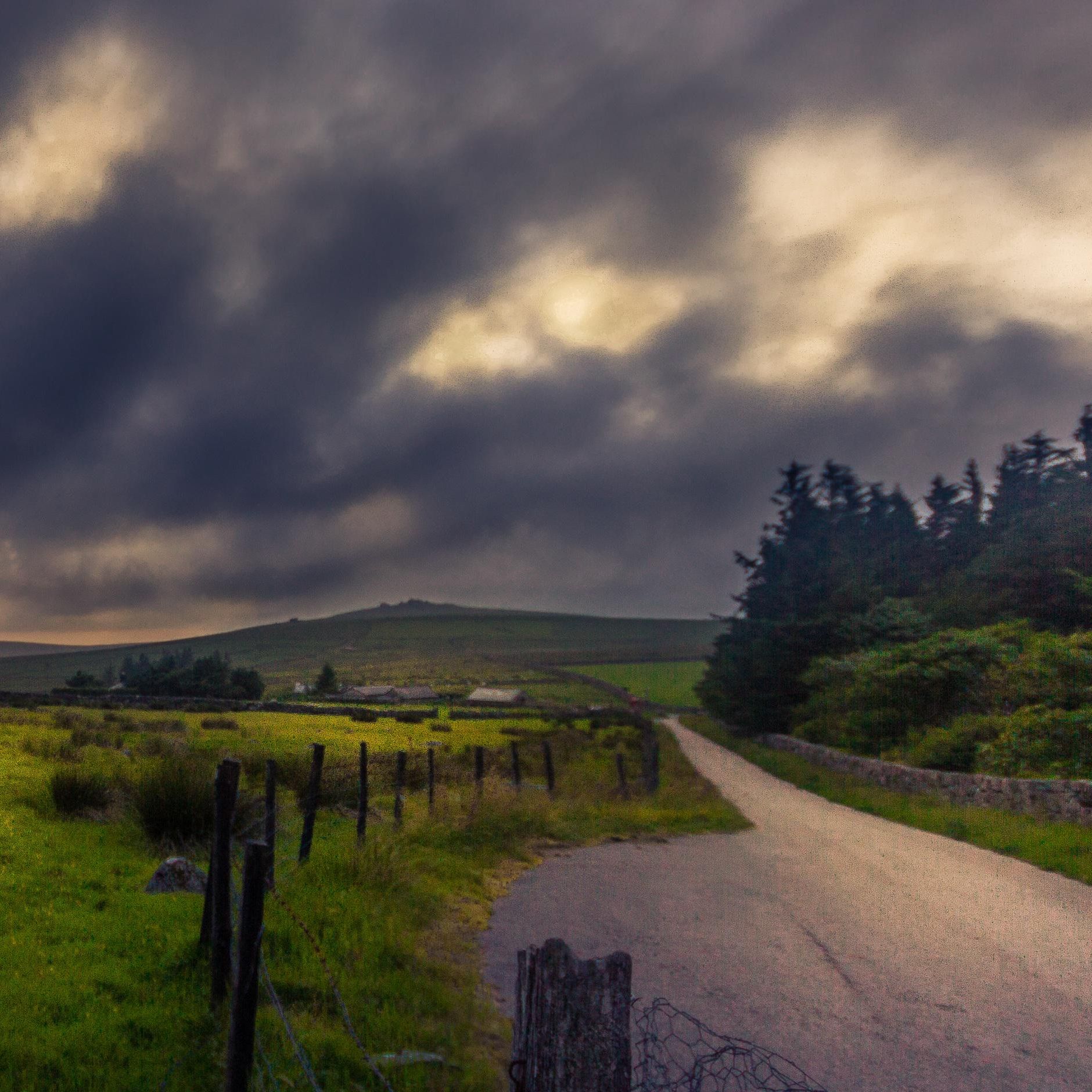 Stormy clouds over a rural landscape with a winding road and stone fence
