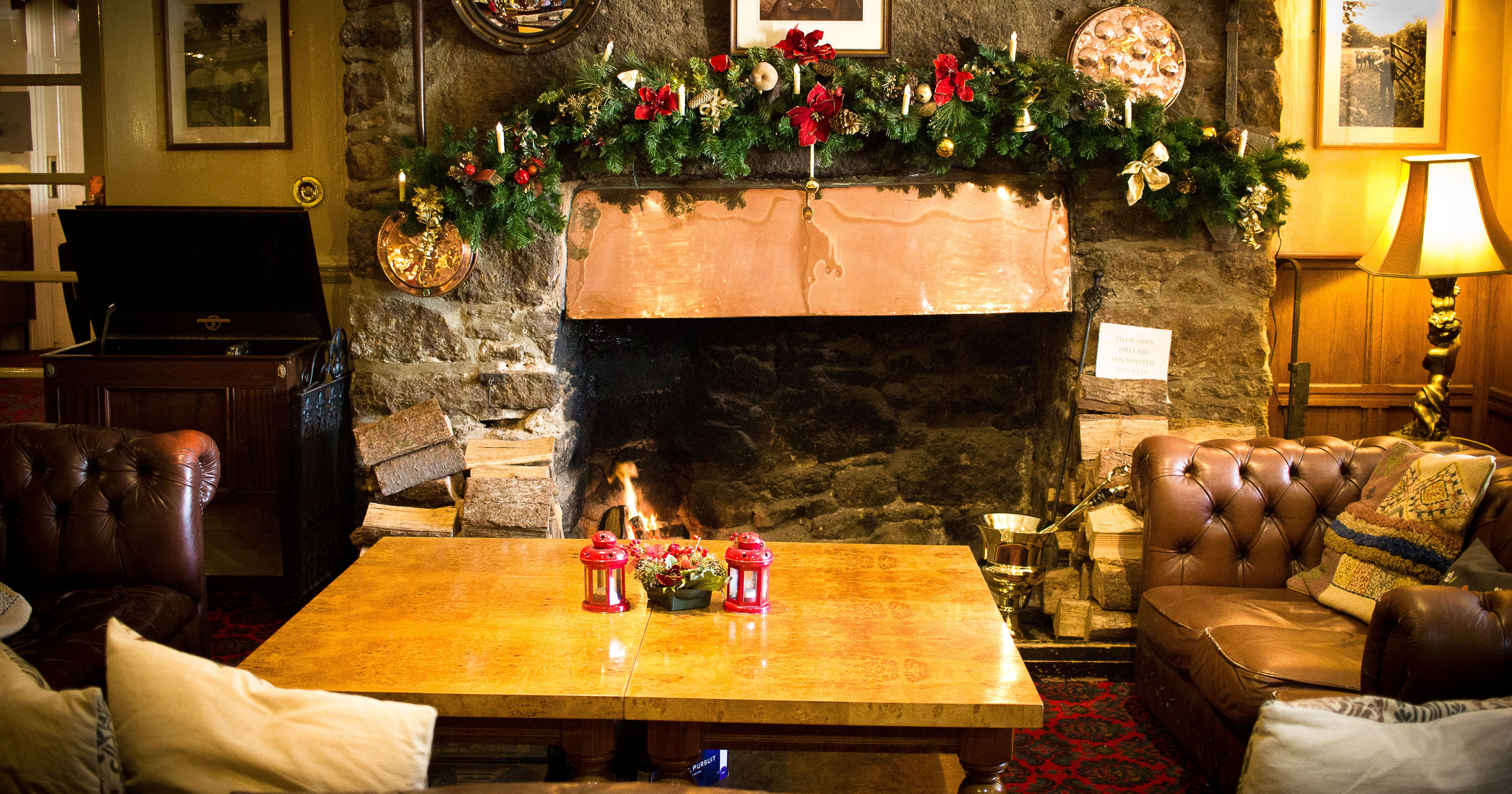Cozy living room with a stone fireplace decorated for Christmas, featuring a copper mantel, festive garland, and vintage furniture.